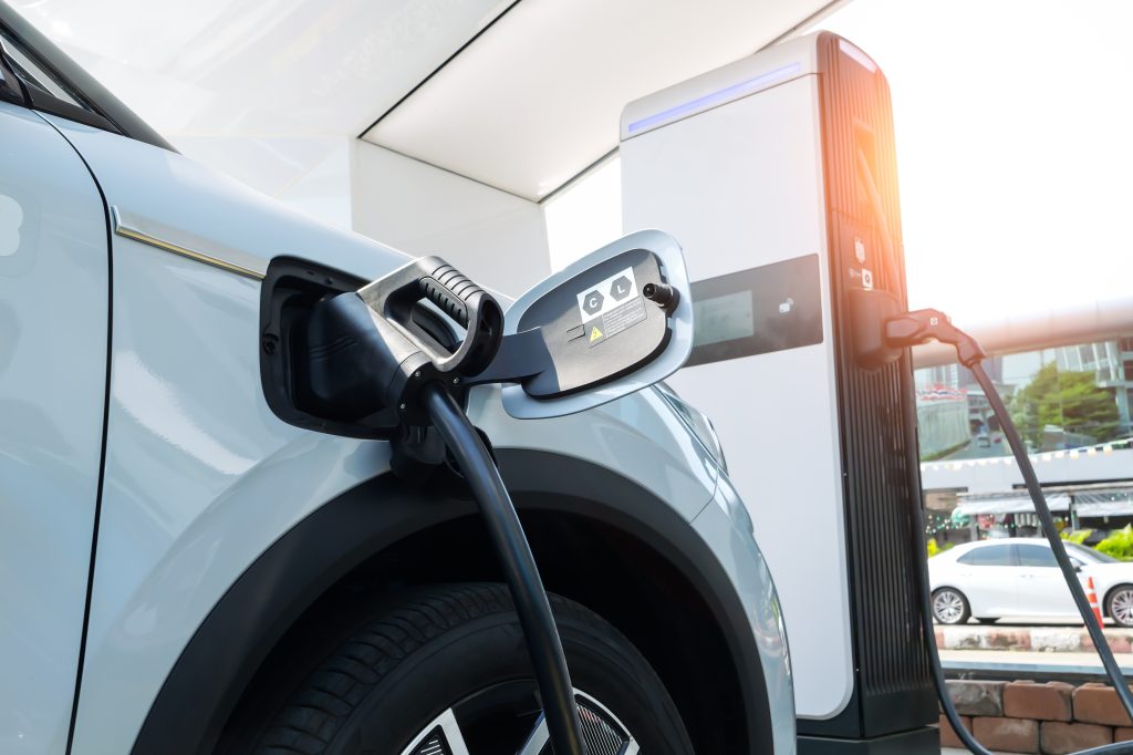 A close-up of an electric vehicle being charged at a charging station, with the charging cable plugged into the car.